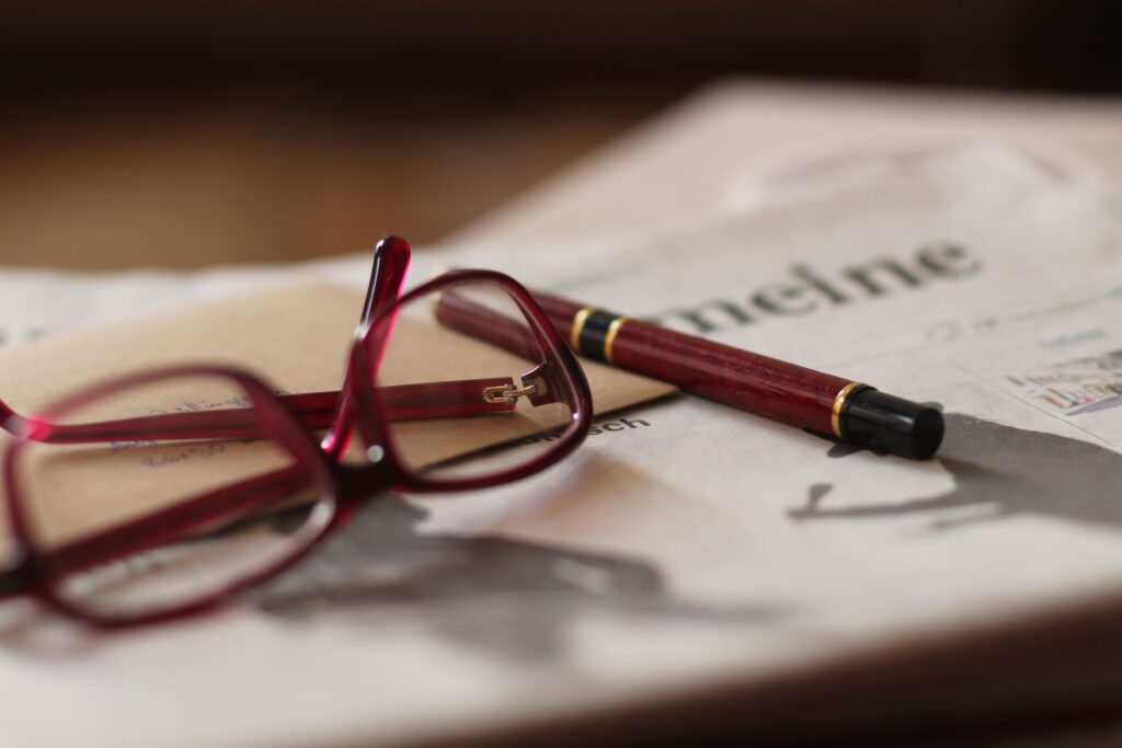 A fountain pen and reading glasses rest on a newspaper, emphasizing a classic reading setup.